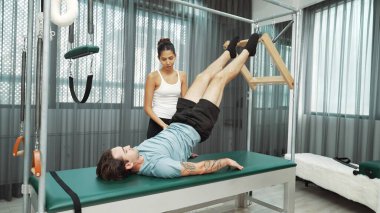 Cadillac ekipmanları üzerinde bacak kaldırma egzersizinde müşteriye yardımcı olan yetenekli pilates eğitmeni. Kadın antrenör, Cadillac 'ın bacak gerdirme hareketine yardım ediyor. Temel bağlantıyı geliştirmek için, bacak esnekliği için. Alışkanlık.