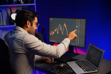 Akıllı tüccar işadamı, karanlık oda gecesinde neon ışıklı ofisteki arama pazarında yüksek kârla ekranda bilgisayar ve bilgisayar üzerinde dinamik borsa yatırımları üzerinde yoğunlaşıyor. Tahmin et..