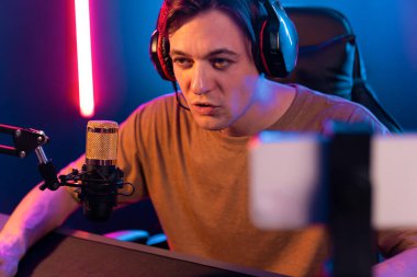 Oyun kanalı, online oyun oynayan akıllı flamalı oyun sunucusu, kulaklık takan, neon ışıklandırma odasındaki takım oyuncusuyla akıllı telefondan canlı yayında konuşan izleyiciler. Bireysel.