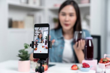 Seçici odaklı akıllı telefon ve gülümseyen genç, güzel Asyalı karışık çilek ve kiraz suyu detoksu değerlendirmesi sosyal medyada sağlıklı ürün tanıtımı sunuyor. Taktik.