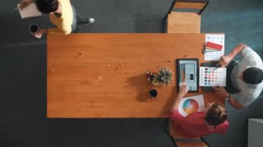 Renk paletinden renk seçmek için birlikte çalışan iş adamlarının üst düzey hava görüşü. İşadamı logo grafiğine bakarken pazarlama ekibine tablet kullanarak yönetici fikri sundu. Sempozyum.