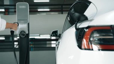 Yavaş çekim kadın, EV elektrikli arabasıyla şehir merkezindeki alışveriş merkezinin otoparkına gidiyor. Sürdürülebilirlik yaşam tarzını yeşil, temiz, yeniden şarj edilebilir elektrikli araç iç organlarıyla şarj ediyor.