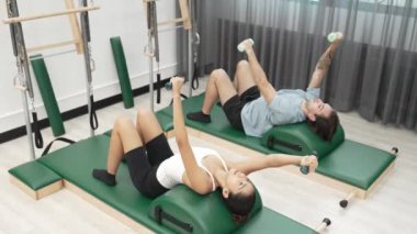 Müşteriler pilates ark fıçısı ekipmanları üzerinde küçük ağırlıklar kullanarak kol ve bacak esnemeleri yapıyorlar. Antrenörlerden bir kaçı sırt, kol ve bacak ağırlıkları ile çekirdeği ve dengeyi geliştiriyor. Alışkanlık.