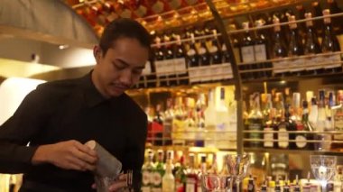 Gülümseyen Asyalı akıllı barmen, lüks tezgah barında bardakla karışık kokteyl hazırlıyor, VIP müşteriyle birlikte gece hayatı sıcak gece kulübü servisinde özel bir içecek hazırlıyor. Vinosity.