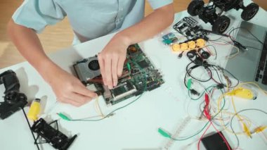 Masadaki elektronik aletle ana kartı tamir eden çocuğa yakın çekim. Elektronik ekipmanlı bir lise öğrencisi elektrik panosunun en üst görüntüsü, kablo aletleri masanın etrafına saçılmış. Öğretim