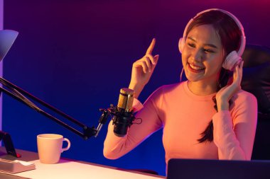 Genç ve güzel Asyalı yayıncının sunucu kanalı, dinleyicilerle sosyal medyada müzik dinliyor, pastel kulaklık takıyor, kapalı alanda neon ışıklı stüdyoda şarkı söylemek için mikrofon kullanıyor. Taktik.