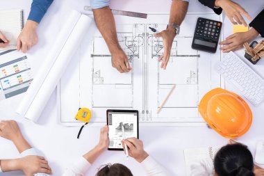 Mimari proje üzerinde birlikte çalışan, inşaat planını gözden geçiren ve toplantı masasında plan oluşturan çeşitli inşaat mühendisi ve müşteri gruplarından oluşan üst düzey bir pankart. Tedbirli