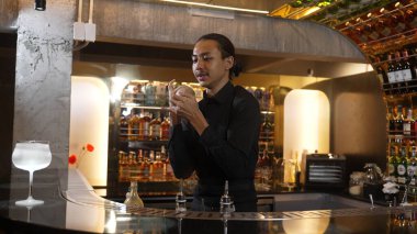 Asyalı akıllı barmen karışık kokteyl sallayarak lüks tezgah hazırlıklarına hazırlanıyor, kameranın önüne bakarak özel bir içecek hazırlıyor. Özel gece hayatı lüksü. Vinosity.
