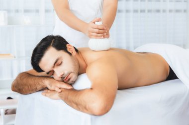 Sıcak bitkisel top spa masaj vücut tedavisi, masör erkek vücuduna nazikçe şifalı bitki torbası bastırıyor. Aromaterapi dinlenme sükuneti ve sükuneti kaplıca salonundaki atmosferi aydınlatıyor. Sessiz.