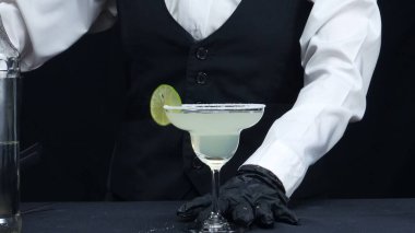 Profesyonel barmen taze margaritayı tuzlu garnitür bardağıyla süslüyor. Yetenekli barmen ellerinin makrografisi barda siyah arkaplanlı kokteyl yapmaya hazırlanıyor. Ağır çekim. Geliştirilebilir.