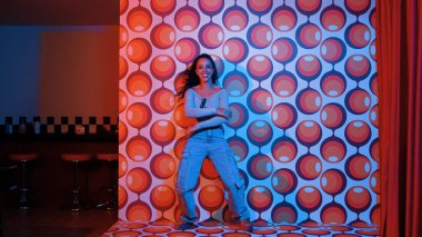 Sıradan tişörtlü bir sokak dansçısı parti sahnesinde canlı bir şekilde kameraya bakarken serbest stil müziğe geçiyor. Sanatçı dans ediyor, enerjik hareketler ve ayak sesleri sergiliyor. Tam vücut. Mutluluk.