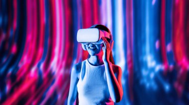 Zeki bir kadın, metaevreni birbirine bağlayan VR kulaklık takan neon ışıklarla çevrili duruyor. Gelecekteki siber uzay topluluğu teknolojisi. Uzaklara bakan zarif bir kadın ve tatmin edici bir şekilde gülümsüyor. Halüsinasyon.