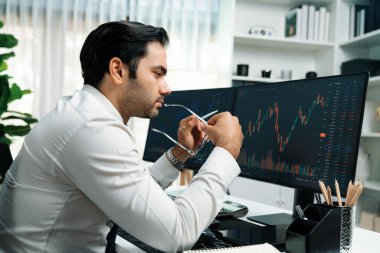 Akıllı tüccar işadamı, modern merkez ofisindeki araştırma pazarında en yüksek kârlı finansal teknolojiye yatırım yaparak bilgisayar üzerinde iki dinamik borsa yatırım ekranını analiz ediyor. Tahmin et..