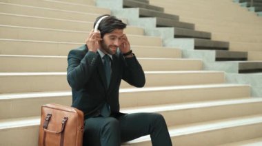 Profesyonel iş adamlarının yakınları kulaklık kullanarak müzik dinlemeyi severler. Akıllı proje yöneticisinin portresi merdivenlerde otururken kulaklık takıyor. İyi haberler almak, terfi almak. Sevinçli..