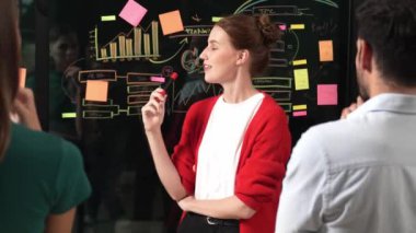 Profesyonel iş kadını yapışkan notlar ve grafikler kullanarak kendine güvenen bir iş kadını sunar. Cam duvarda istatistiksel grafikle duran yetenekli genç ve güzel proje yöneticisi. İzleme