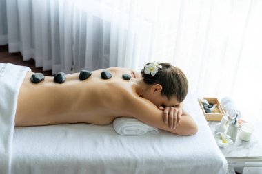 Lüks tatil köyündeki kaplıcalarda sıcak taş masajı. Gün ışığı sükunet ortamında, mutlu kadın müşteri bazalt taş masajından zevk alıyor. Rahatlatıcı bir sıcaklıkla vücudun üzerinde süzülüyor. Sessiz.