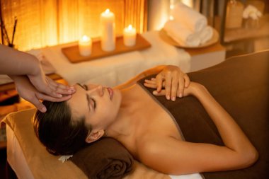 Beyaz kadın stres önleyici kafa masajı yapmaktan ve lüks otel veya otelde sıcak mum ışığında yüz güzelliği eğlencesi yapmaktan zevk alıyor. Sessiz.