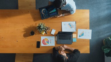 Meslektaşı tabletten rapor veya mali grafik gösterirken proje yöneticisinin dizüstü bilgisayarda çalışmasına ilişkin üst görünüm. Toplantı masasında elinde not ve dizüstü bilgisayarla oturan erkek lider. Cemaat.