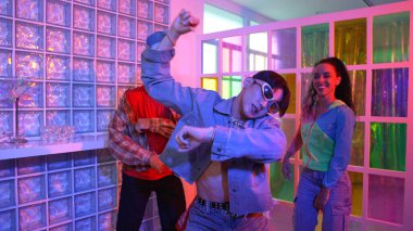 Asyalı adam gece kulübünde çeşitli neon ışıklarda dans ederken kolunu oynatıyor. Modern kulüpte çok kültürlü hippilerle dans eden şık elbiseli mutlu dansçı. Mutluluk.