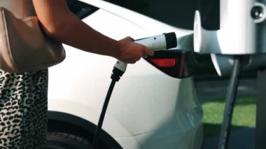 Genç bir kadın, yeşil sürdürülebilir şehir parkı bahçesinde elektrik yüklü EV arabasıyla geziyor. Sürdürülebilir kentsel yaşam tarzında, yeniden şarj edilebilir elektrikli araç iç organlarıyla alışveriş yapmak için.