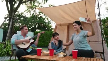 Baba gitar çalarken anne ve kızı bahçede kamp yapıyor. Ebeveynler, genç nesil çapraz kuşak farklılıklarıyla zaman geçirmek için açık hava kamp aktivitelerini kullanıyorlar. Uyumsuzluk.