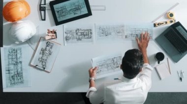 Proje planını kontrol ederken ve seçerken mimar mühendisin bina planlarını masaya yerleştirdiği tepeden aşağı hava görüntüsü. İç mimar toplantı masasından mimari plan seçti. Hizalama.