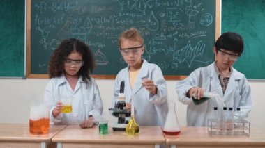 Çocuklar laboratuvarda karatahta başında dururken fen dersinde deney yapıyorlar. Mutlu öğrenci biyokimyasal sıvıyı keşfederken ve incelerken ve karıştırırken. Pedagoji.