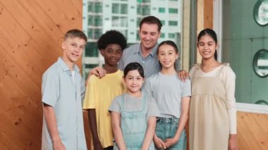Mutlu öğretmen ve çeşitli öğrenciler kameraya gülümserken ayakta duruyorlar. Profesyonel akıllı eğitmen ve karışık ırk olan lise öğrencileri kameraya neşeli pozlar veriyor. Öğretim