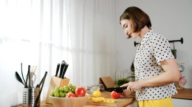Enerjik anne, mutfak malzemeleri ile çevrili sebzeleri doğrarken modern mutfakta kahvaltı için salata yapıyor. Akıllı kadın temizlikçi yemek pişirir ve yemek hazırlar. Sağlıklı bir yaşam tarzı. Pedagoji.