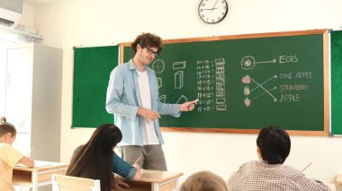 Öğrenciye bakarken, sınıfta matematik teorisi hakkında konuşan ve açıklayan beyaz bir öğretmen. Tahtanın önünde durup tahtaya işaret eden yetenekli bir eğitmen. Pedagoji.