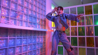 Gece kulübünde kameraya bakarken güneş gözlüklü Asyalı dansçı serbest dans ediyor. Mutlu sokak dansçısı dans ediyor ve renkli parlak neon ışığı ya da yol gösteren ışıkla ayak seslerini gösteriyor. Mutluluk.