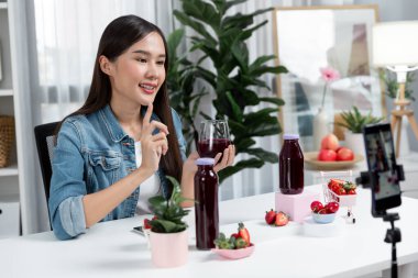 Gülümseyen, güzel Asyalı genç, lezzetli karışık çilek ve kiraz suyu detoksu içeceklerini inceleyen, sosyal medyada özel promosyon satışı için sağlıklı ürünler sergileyen. Taktik.