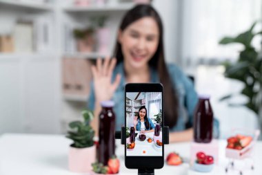Seçici odaklı akıllı telefon ve gülümseyen genç, güzel Asyalı karışık çilek ve kiraz suyu detoksu değerlendirmesi sosyal medyada sağlıklı ürün tanıtımı sunuyor. Taktik.