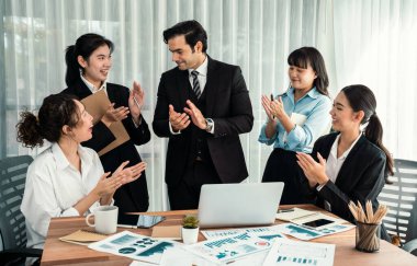 Kutlama jesti ve başarılı takım çalışması yapan bir grup mutlu iş adamı. Çeşitli yarış bürosu çalışanları şirket ofisinde pazarlama planlamasında ilerleme kaydettikten sonra kutlama yapıyorlar. Habiliment