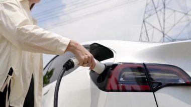 Alt görüşlü kadın EV araba aküsünü şarj ediyor elektrik şebekesine bağlanıyor elektrik endüstrisi çevre dostu araç için elektrik endüstrisi olarak. Yararlı