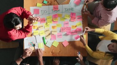 Renkli yapışkan notlarla plan yazarken ve planlarken insanların çalışma tahtası ya da kanban yönetim kurulu oluşturma ve yazma stratejilerinin en üst görünümü. Takım el ele tutuşup alkışlıyor. Cemaat.