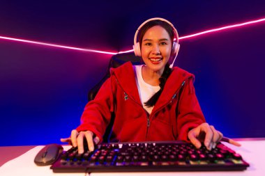 İnternet üzerinden kulaklık takıp gülümseyen Asyalı güzel kız flamasının sunucu kanalı izleyicilerle internet üzerinden konuşma yapıyor. Esport yetenekli takım oyuncuları neon mavi odada. Taktik.