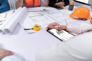 Mimari proje üzerinde birlikte çalışan çeşitli inşaat mühendisi ve müvekkil grupları, inşaat planını gözden geçirip toplantı masasında plan oluşturuyorlar. Tedbirli