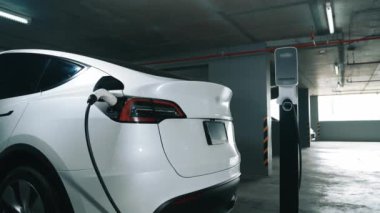 Şehir merkezindeki kapalı otoparkta yavaş çekimde EV elektrikli araba şarj oluyor. Şehir merkezinde sürdürülebilirlik yeşili, yeniden şarj edilebilir elektrikli araç iç organları.