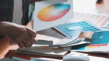 Toplantıda profesyonel tasarımcı yazma ve logo grafiği tasarlama. Renkli paletler üzerinde çalışan iş adamlarının yakınlaşması ve masaya kağıt ve ekipman ile yapışkan notlar yazmak. Sempozyum.