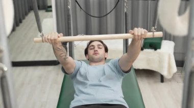 Adam spor salonundaki kol ve vücut kaslarını güçlendirmek için pilates trapez çubuğunda çekirdek egzersizi yapıyor. Göğüs ve omuz güçlendirmek için Cadillac 'a göğüs presi yapan antrenör. Alışkanlık.