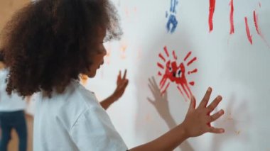 Çeşitli öğrenciler resim dersinde duvardaki boyanmış renklerle el ele tutuşuyorlar. Mutlu çok kültürlü arkadaşlar oyun oynuyor ve duvarları boyadıkları yaratıcı aktivite konseptinin tadını çıkarıyorlar. Etkinlik.