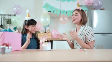 Çocuk ve beyaz anne birlikte doğum günü şarkısı söyleyip mumu üflüyorlar. Asyalı kız ve beyaz anne doğum gününü renkli balon ve hediyelerle süslenmiş yemek salonunda kutluyor. Pedagoji.