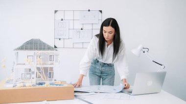 Genç, güzel beyaz bir mimar masanın üzerine plan koyar ve ev modeliyle karşılaştırırken, modern ofisteki fahişe modellerini dikkatlice incelerken arkadaki çizgilerle karşılaştırır. Tertemiz..