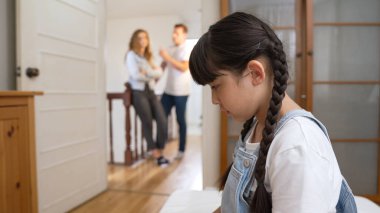 Stresli ve mutsuz genç kız köşeye kıvrılıp kulaklarını kapatarak arka planda ebeveyninin tartışmasını engelliyor. Evde aile içi şiddet ve travmatik çocukluk depresyona dönüşür. Eşzamanlama