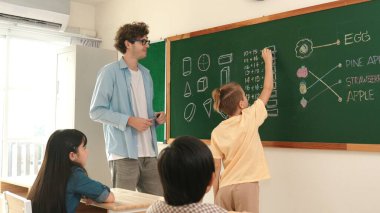 Akıllı çocuk tahtada dururken matematik teorisine cevap yazıyor. Beyaz çocuk sınıfın önünde sınav yaparken çekici erkek öğretmen ilköğretim sınıfına bakıyor. Eğitim. Pedagoji.