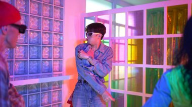 Ortasında dans eden profesyonel mutlu hipster onu alkışlayan çeşitli arkadaşlarıyla dans ediyor. Çekici Asyalı kırığı gece kulübünde neon ışığıyla enerjik adımlar atıyor. Mutluluk.