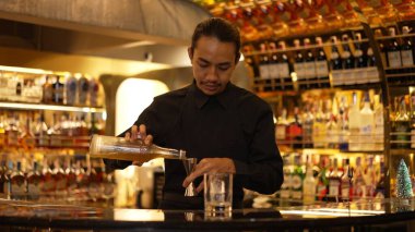 İyi görünümlü Asyalı barmenin içki şurubunu barın lüks içki tezgahında buzlu cama dönüştürdüğü profili. Gece kulübü lüksünde profesyonel barmen kostümü. Vinosity.