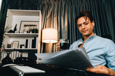 Satış müdürü bilgisayar üzerinde çalışıyor ve modern ev ofisinde gece kahve içerken iş grafiği raporuyla karşılaştırma yapıyor. Çeyrek yıllık sunum karlı ürün için. Bireysel.