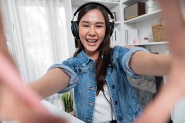 Sunucu kanalı genç ve güzel Asyalı kız akıllı telefonuyla selfie çekiyor. Modern stüdyo ofis konseptinde kulaklık takıyor. Sahne arkası yayıncısı sosyal medyada canlı yayın yapıyor. Taktik.